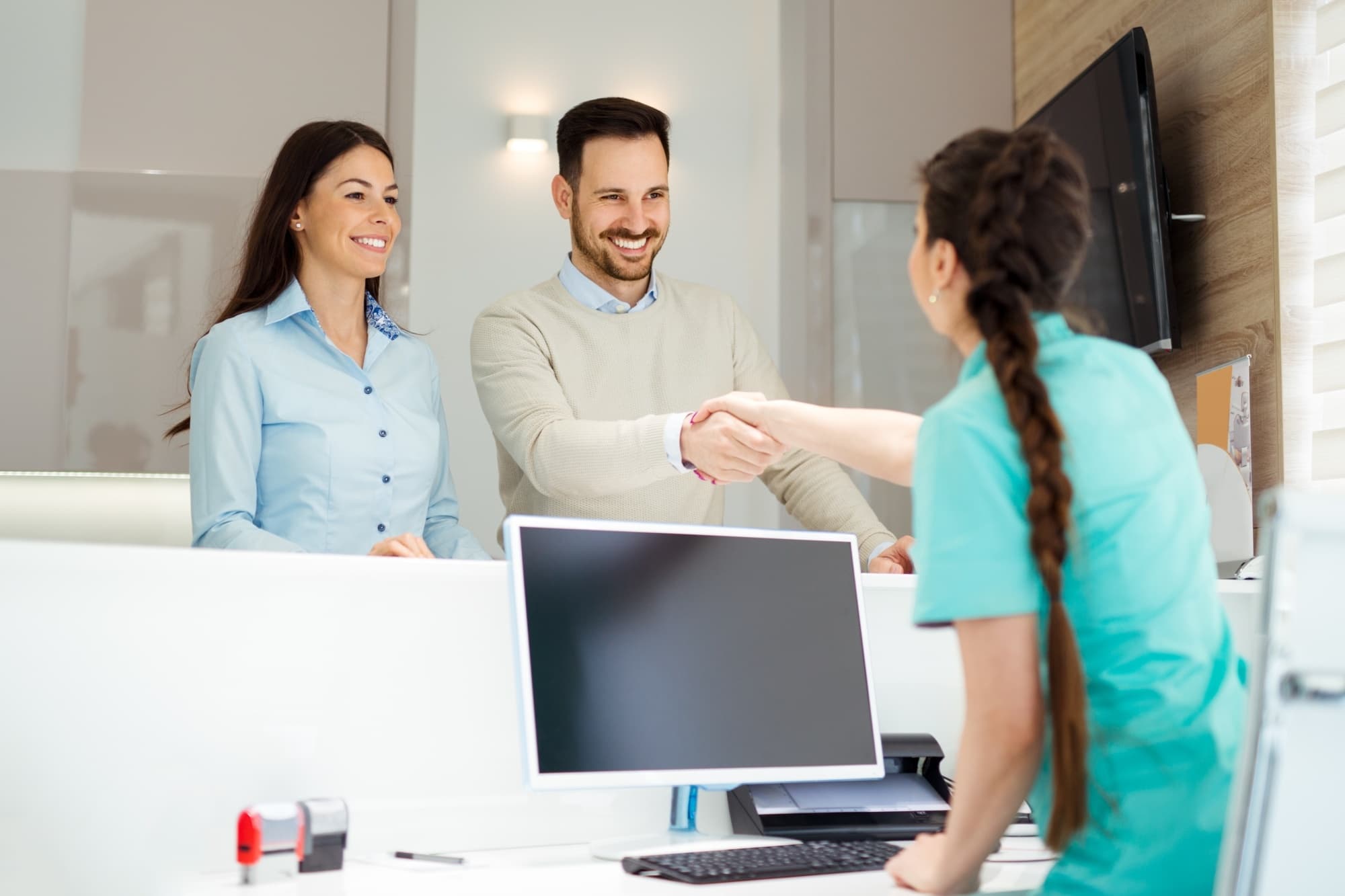 A patient couple greeted warmly by a team member at the front desk