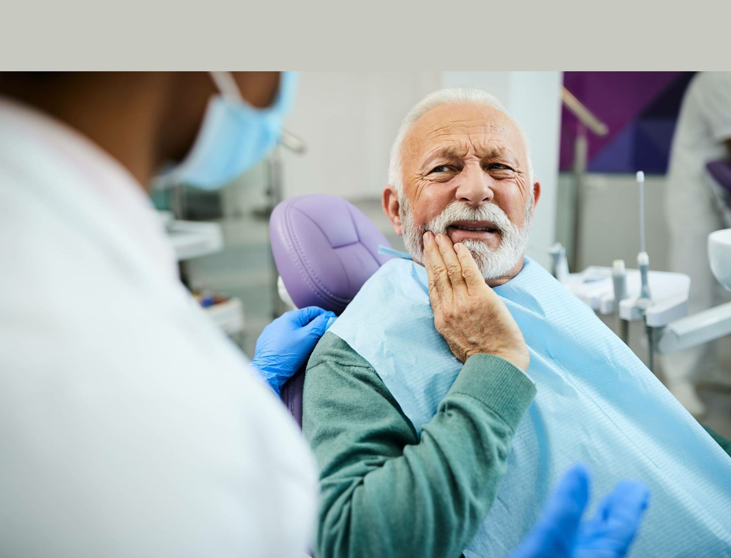 A senior patient wincing in pain, holding his jaw, at the dentist