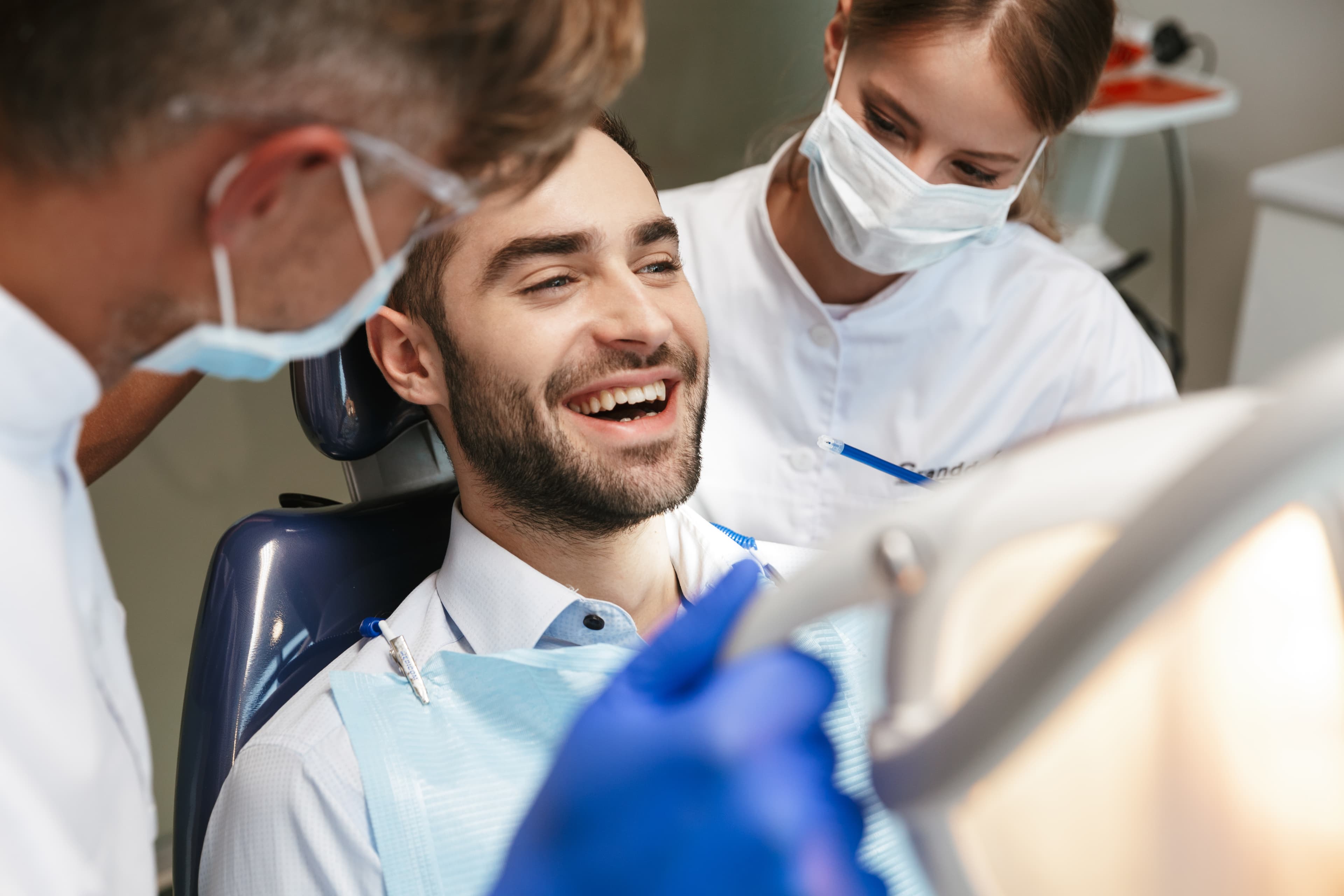 A smiling patient in a dental chair with the dentist and assistant beside him