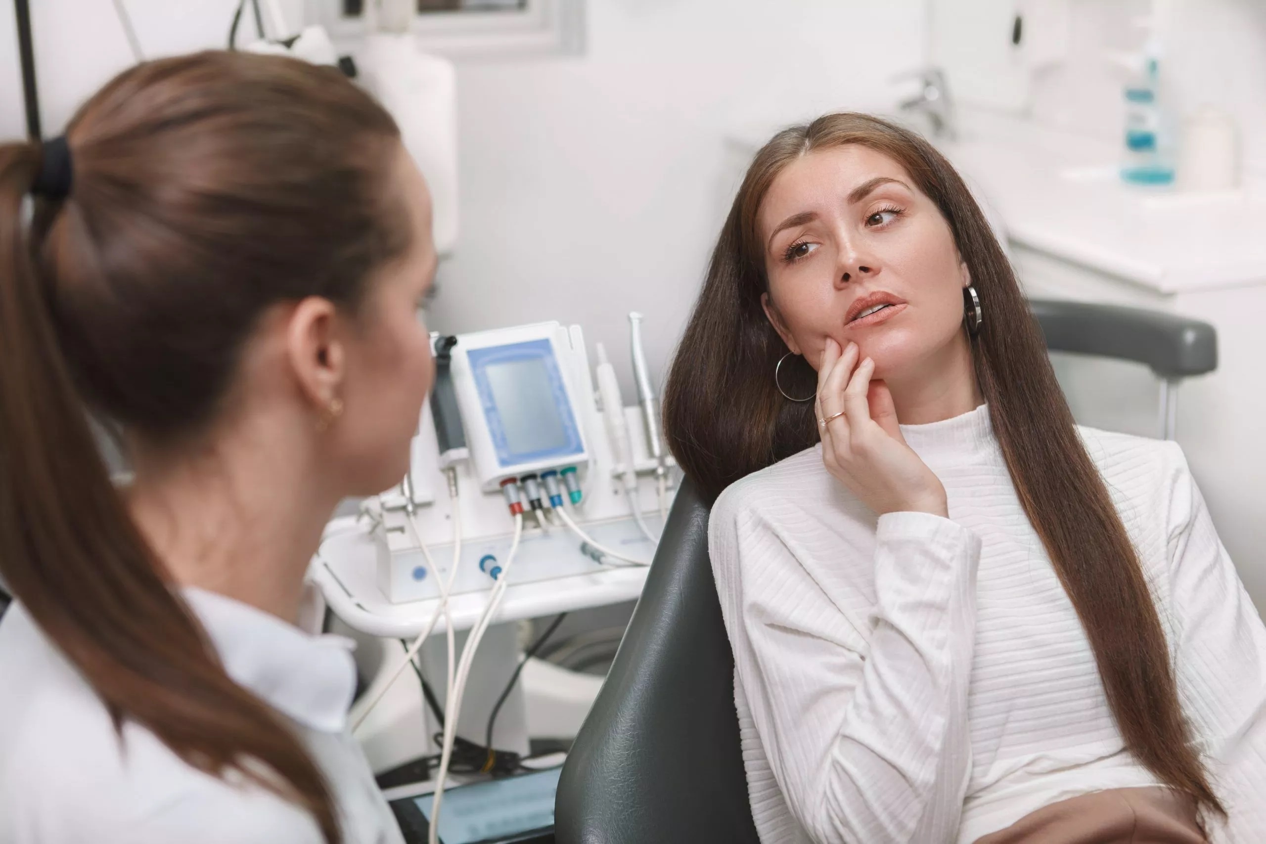 A worried woman holding her jaw in the dental chair