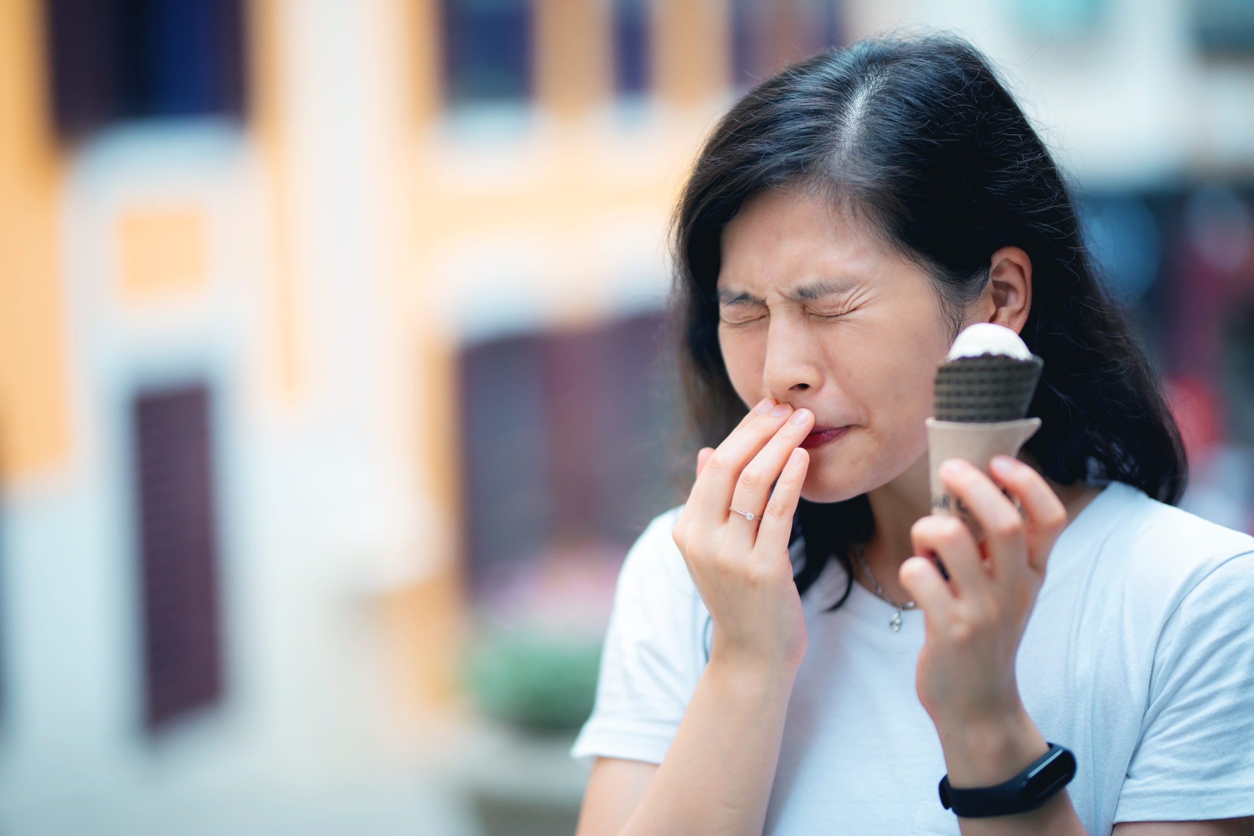 A woman wincing in pain while eating ice cream
